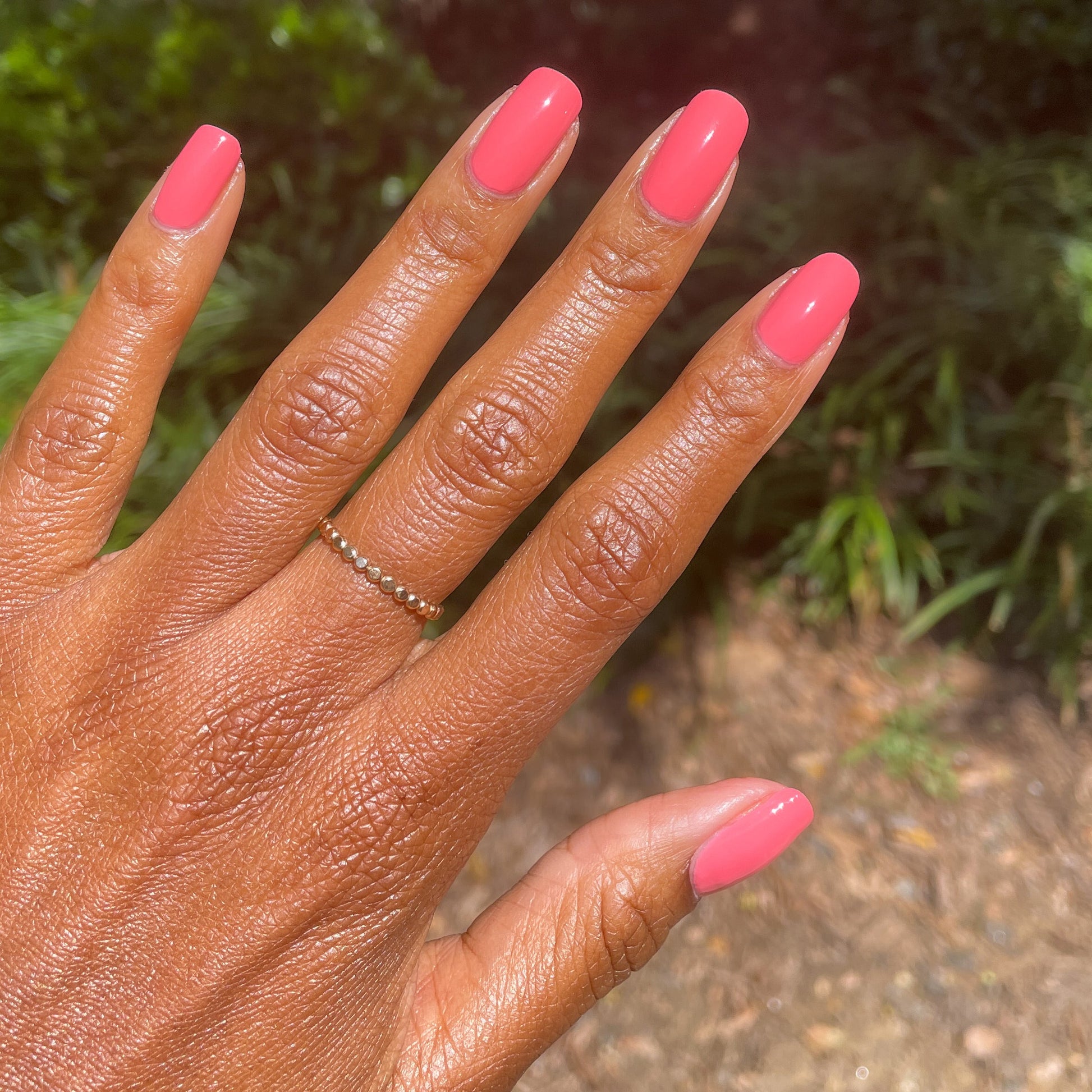 Hand showing nails polished in Stinson Sunset gel polish by Olive and June for a bright manicure outdoors