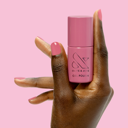 Prom - Gel bottle held between fingers with matching soft pink gel polish for an elegant at-home manicure by Olive and June