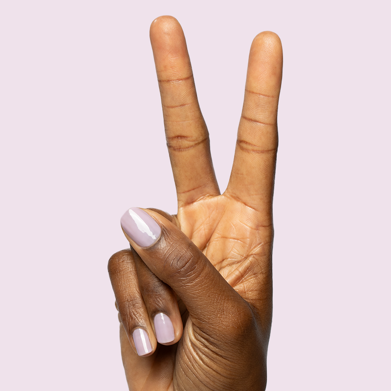 Hand showing peace sign with natural-shaped nails painted in pastel lavender Dreamy gel polish on pale lavender background