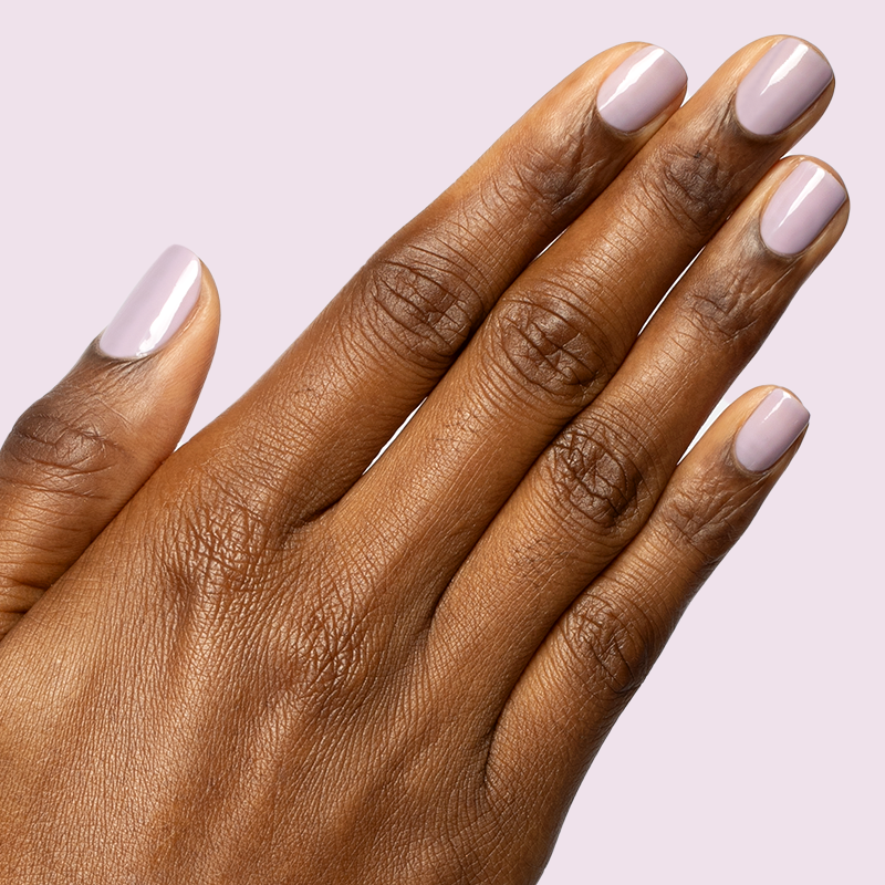 Hand with short rounded nails painted in sheer pastel lavender Dreamy gel polish on light lavender background