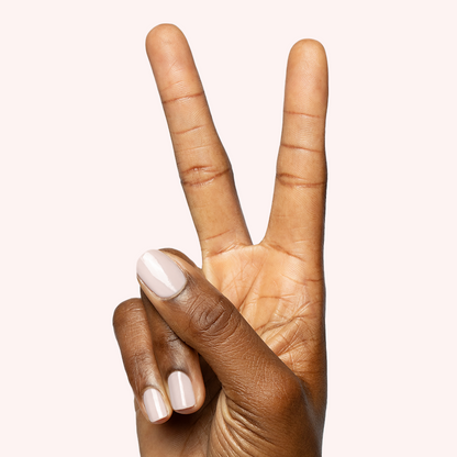 Hand showing peace sign with nails painted in sheer milky pink Puffball quick dry gel polish manicure on pale background