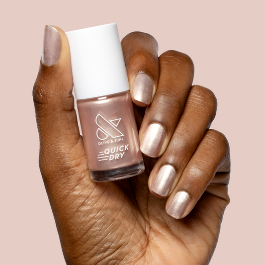 Hand holding Olive and June Supernova polish bottle with nails painted in shimmering sheer pink quick dry manicure color
