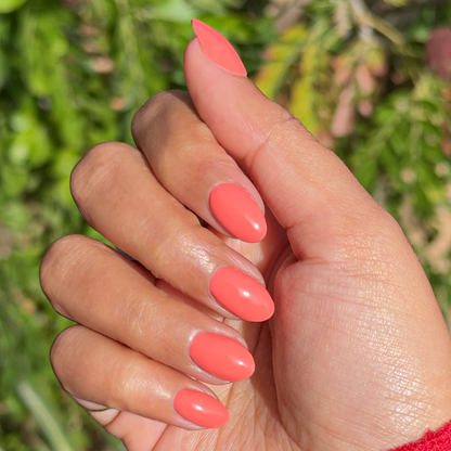 Hand with almond-shaped nails painted coral Ride into the Sunset gel polish in natural light outdoors