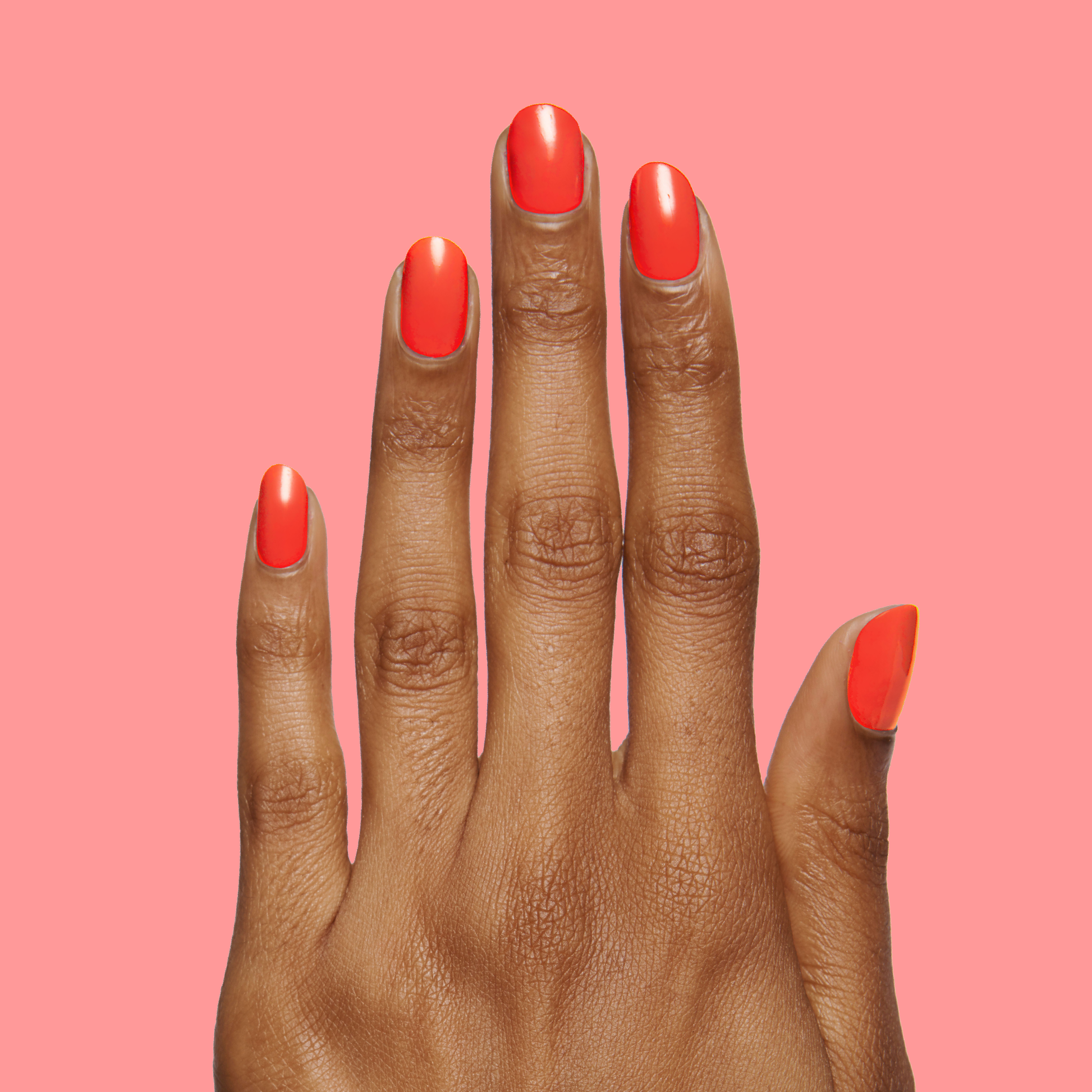 Hand showcasing a smooth, glossy Lava nail polish manicure in vibrant spicy orange-red on coral background