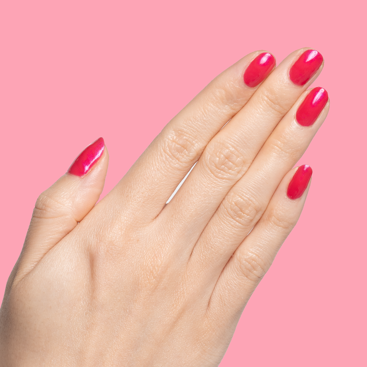 Hand with short nails painted in vibrant Berries gel polish showing smooth, glossy manicure against bright pink background