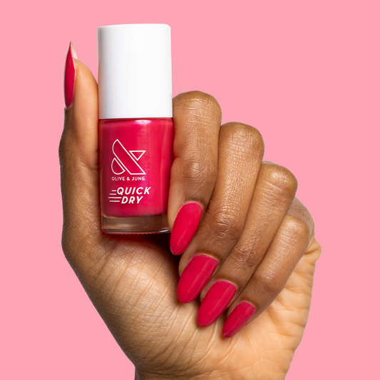 Hand holding Olive and June Berries quick dry polish with matching berry-pink gel mani against soft pink background