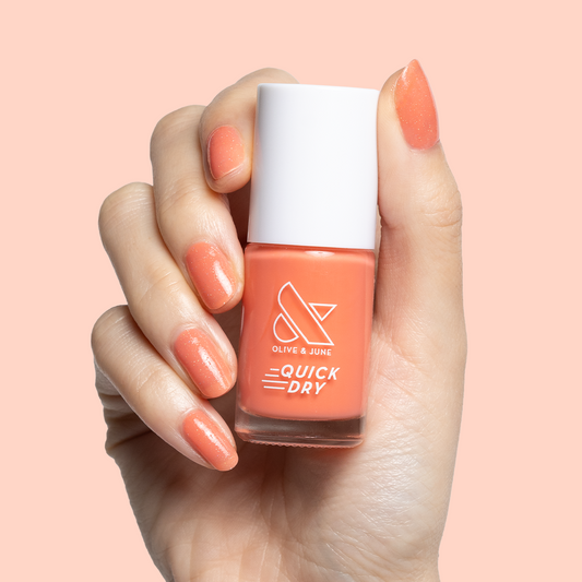 Hand with rounded nails painted in Cape polish holding bottle showing coral pink quick dry mani finish