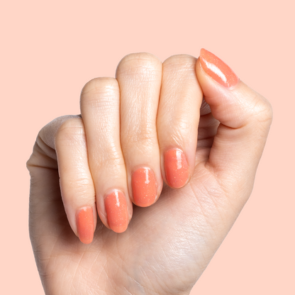 Hand with short nails painted in Cape showing a glossy coral pink manicure perfect for at home manis and pedis