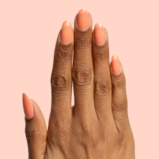 Hand with medium-length nails painted in Cape polish showing smooth coral pink manicure against soft peach background