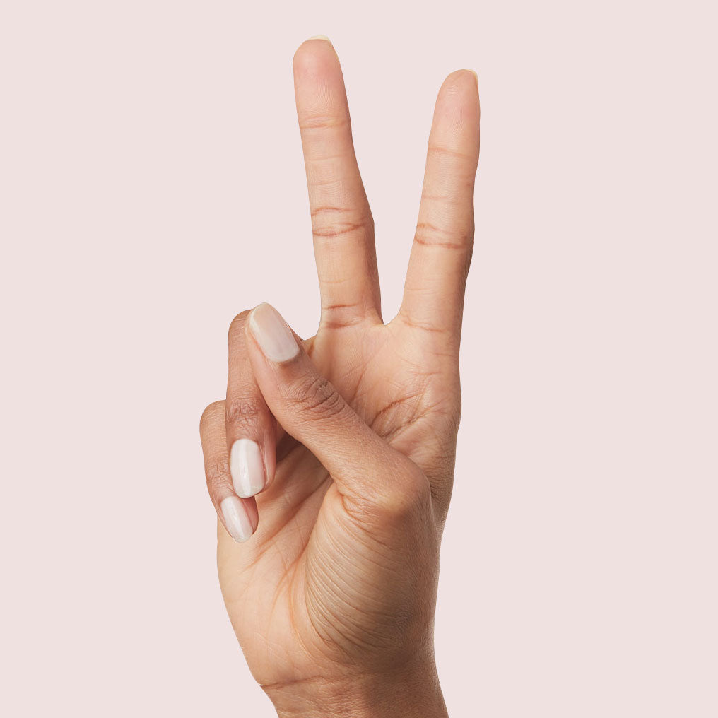 Hand showing peace sign with nails painted in sheer pink Strawberry Scone polish for a natural Olive and June manicure