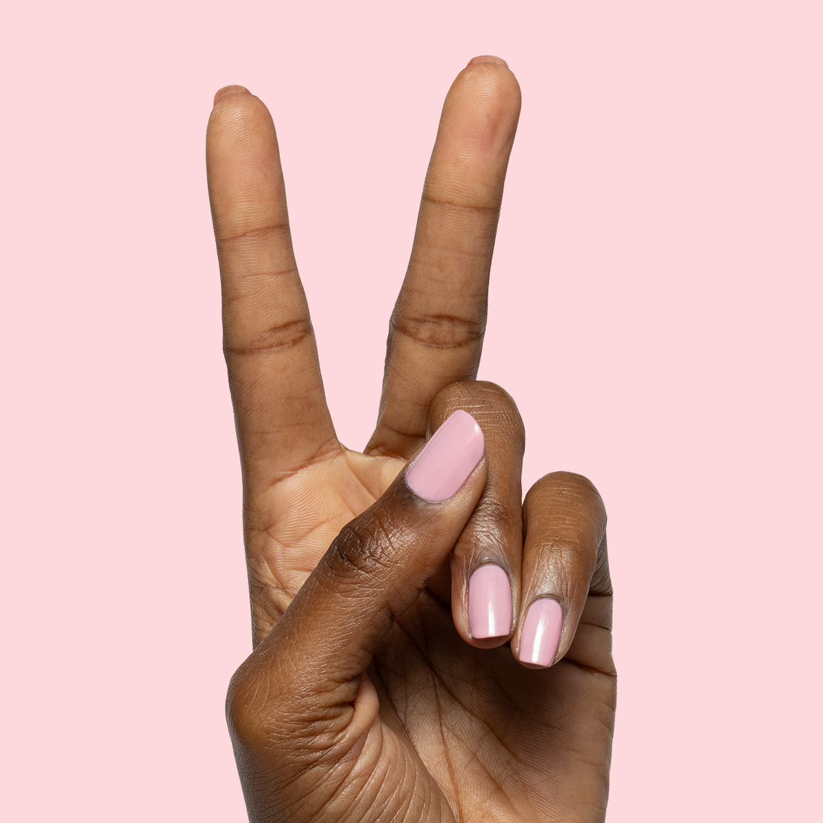 Hand with nails painted in sheer pink Saltwater Taffy gel polish showing polished manicure against pink background