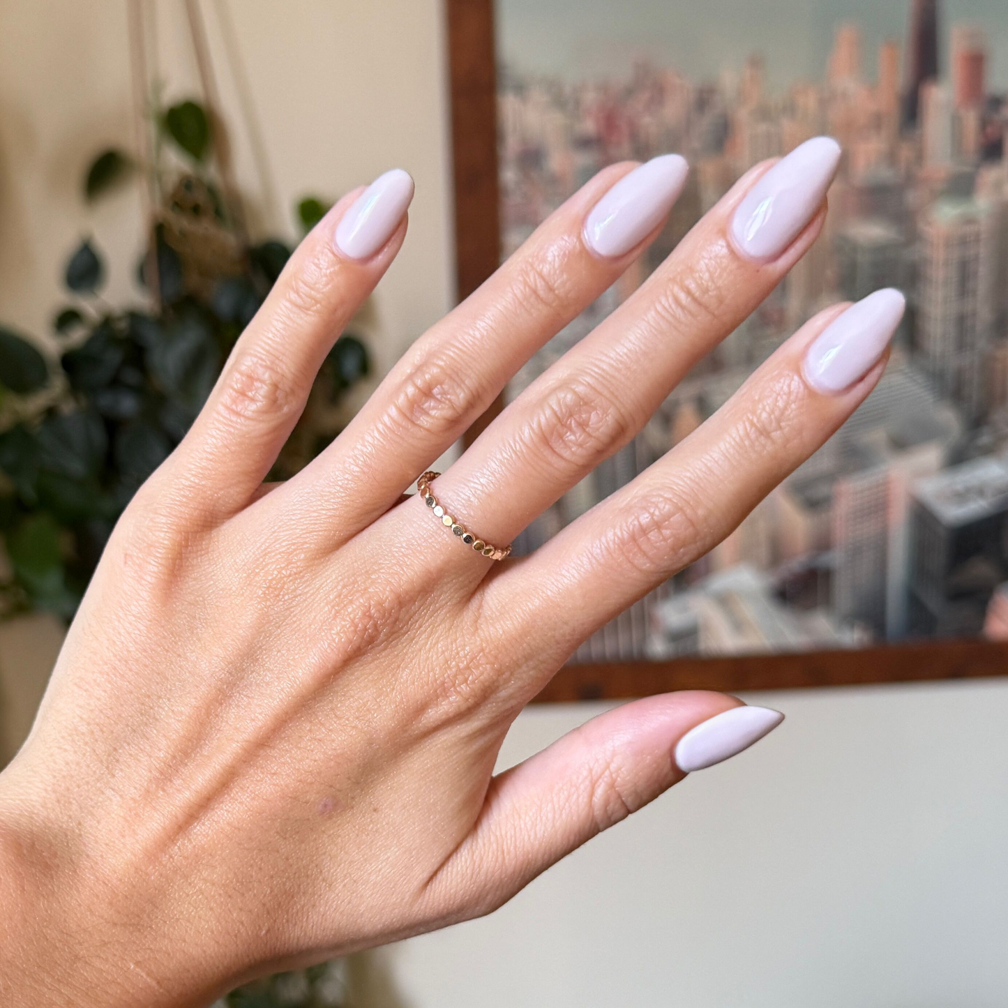 Hand with almond-shaped nails in cool lavender grey Sculpture Wing - Gel polish against blurred cityscape background