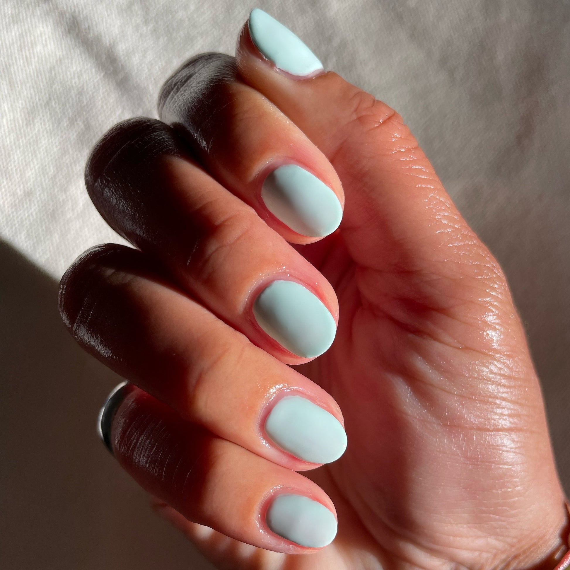 Fingers with nails coated in pastel mint green Sleeping Bag long-lasting polish by Olive and June in natural lighting