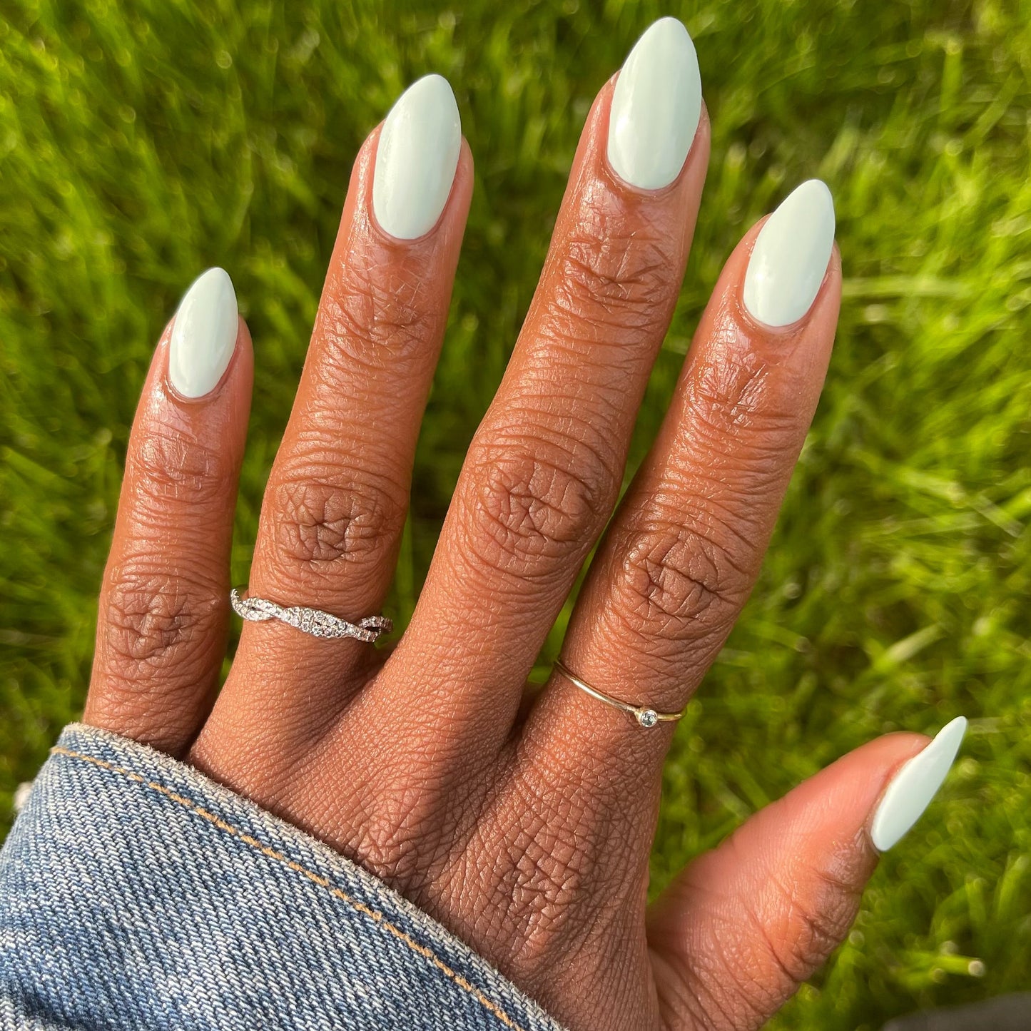 Hand with almond-shaped nails in pastel mint green Sleeping Bag gel polish by Olive and June outdoors on grass background