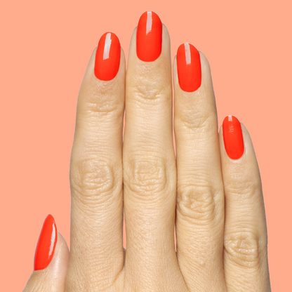 Fingers with medium-length nails painted in bright orange-red Snapdragon quick dry gel polish on coral background