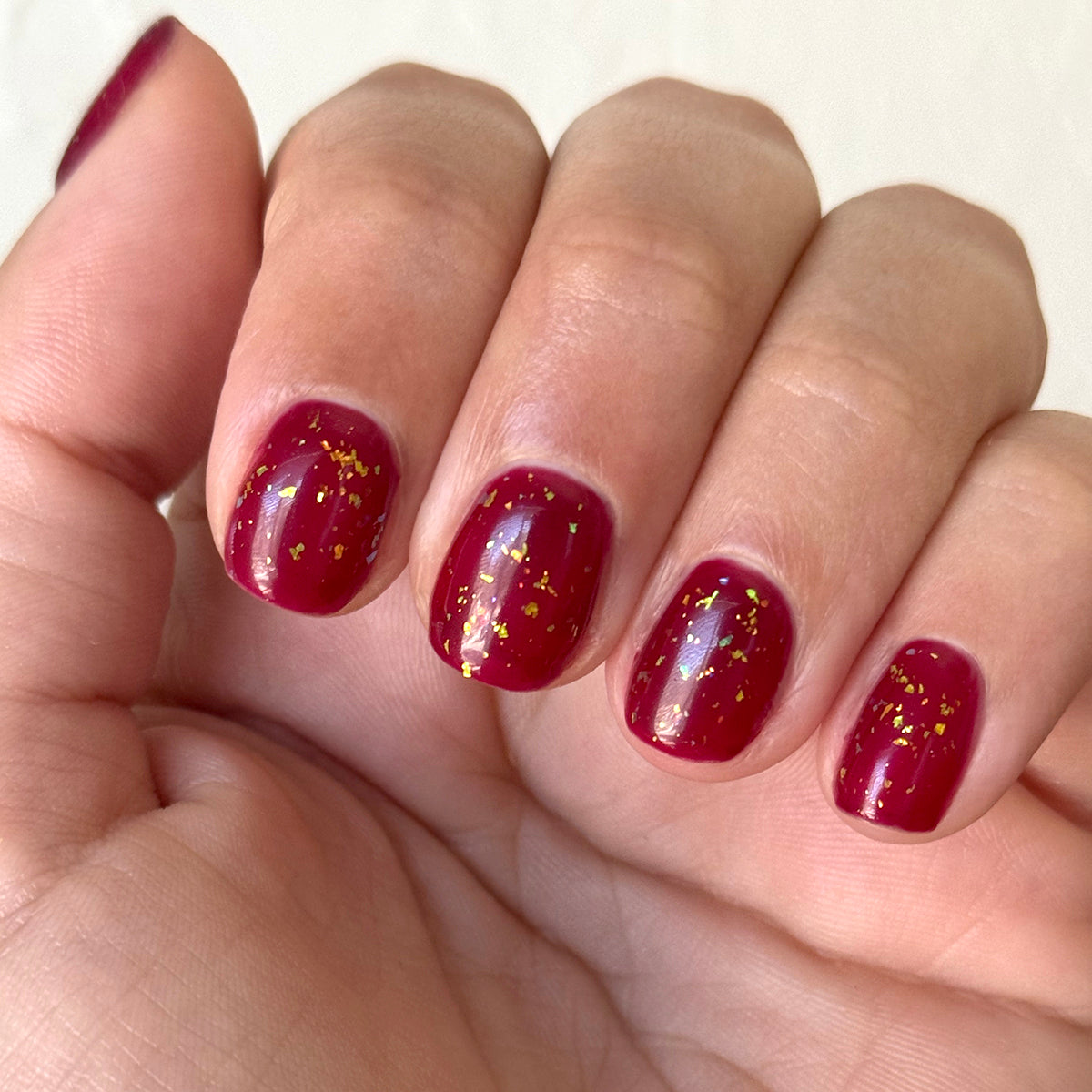 The Stardust Effect Top Coat on rich red polish with scattered gold flakes for a luminous and festive manicure finish