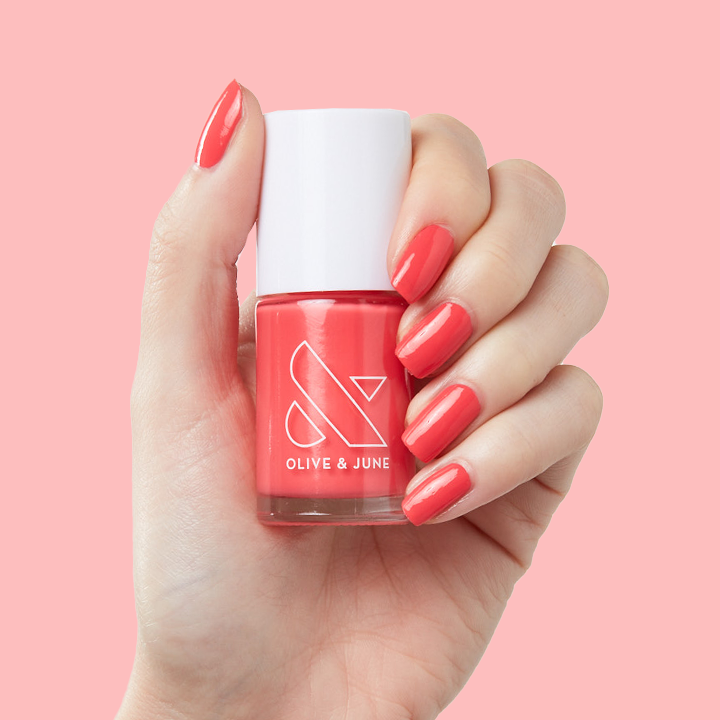 Hand holding a bottle of Field Day nail polish with nails painted in juicy watermelon red polish for a vibrant mani