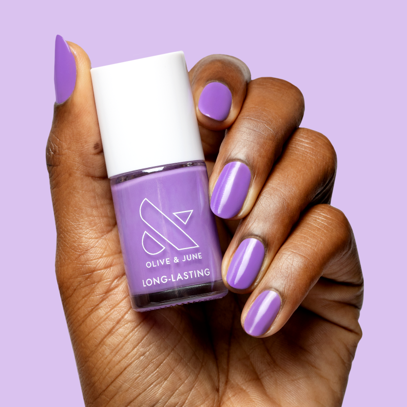 Hand holding a bottle of Tennis Skirt nail polish by Olive and June with matching purple polished nails