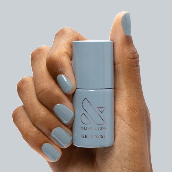 Vintage - Gel polish bottle held with nails painted in a smooth vintage denim blue for a chic manicure by Olive and June