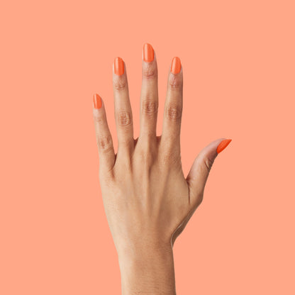 Hand with nails polished in bright tangerine You're a 10 gel polish showing fresh manicure on coral background