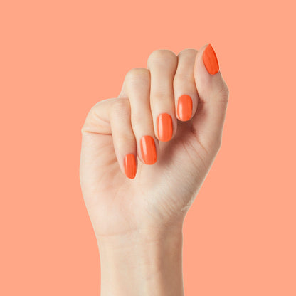 Hand with nails polished in bold tangerine "You're a 10" gel polish showing fresh and glossy manicure on coral background
