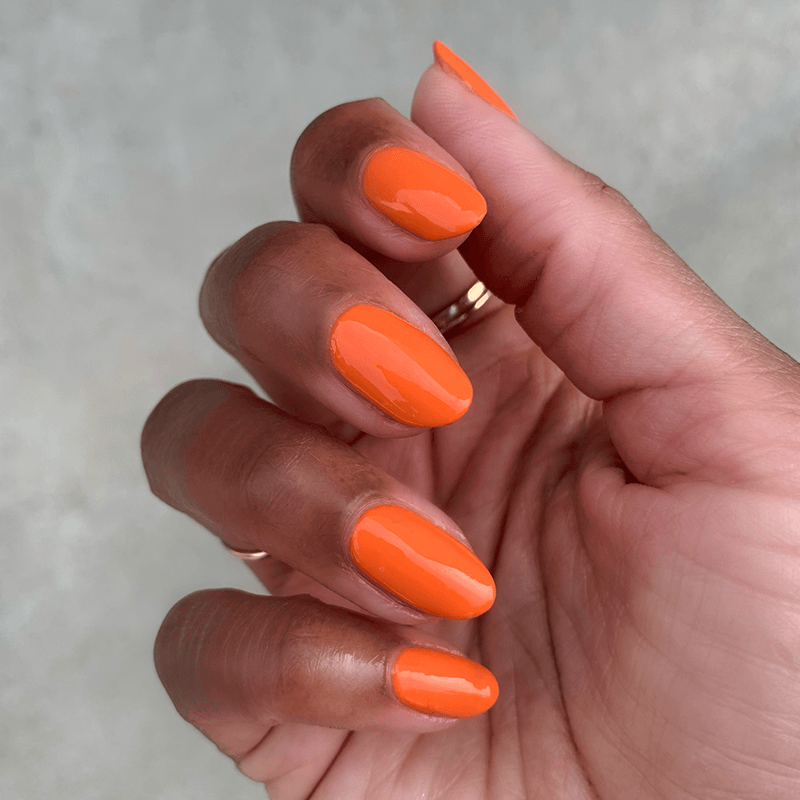 Hand with nails painted in glossy bright tangerine shade "You're a 10" gel polish showing fresh manicure