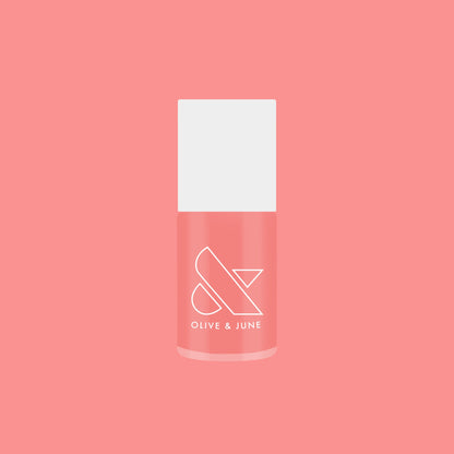 Bottle of Carrot Juice gel polish by Olive and June in a vibrant carrot orange shade on coral background