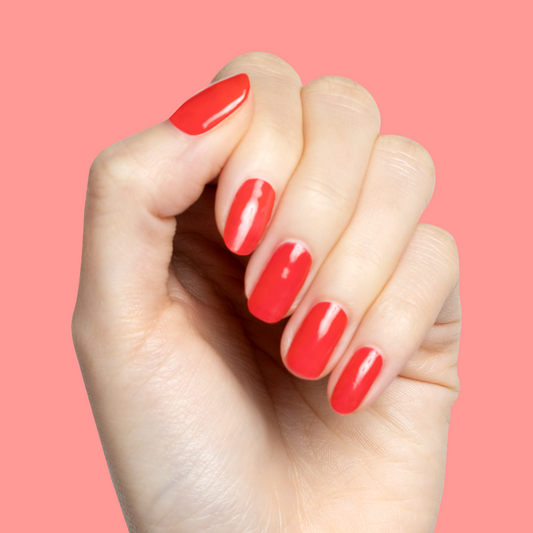 Hand with short nails painted in glossy Fragola strawberry pink polish showing smooth at-home manicure against coral background