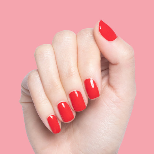 Hand with nails painted in glossy cherry red Lollipop polish against a soft pink background