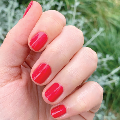 Hand with short nails polished in vibrant Hibiscus showing a smooth and glossy long-lasting mani outdoors