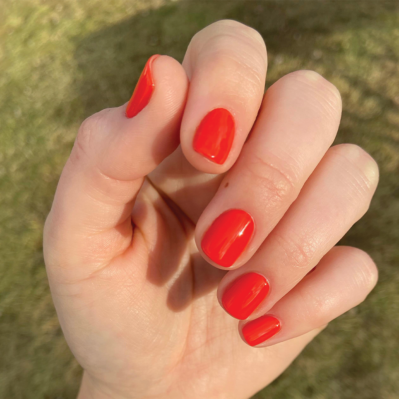 Hand with bright Lava nail polish in spicy orange red showing a smooth, glossy manicure in natural sunlight
