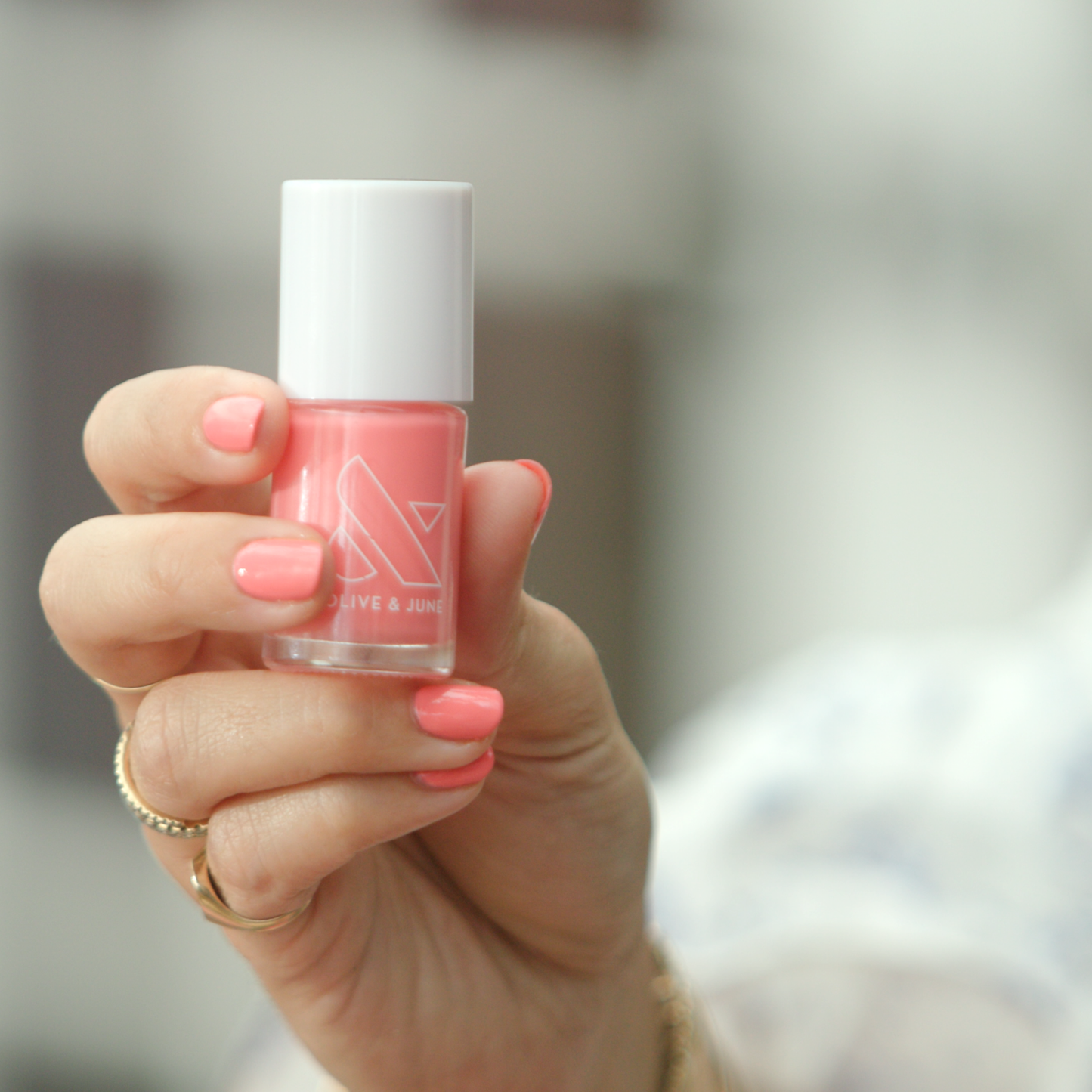 Hand holding a bottle of Stinson Sunset gel polish by Olive and June with matching peachy-pink manicure