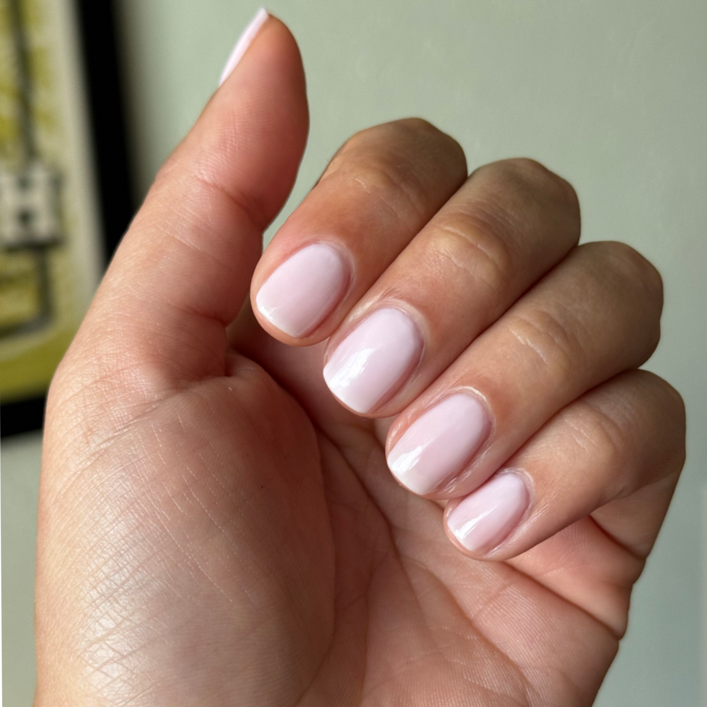 Hand with short nails coated in sheer milky-pink Puffball quick dry gel polish manicure