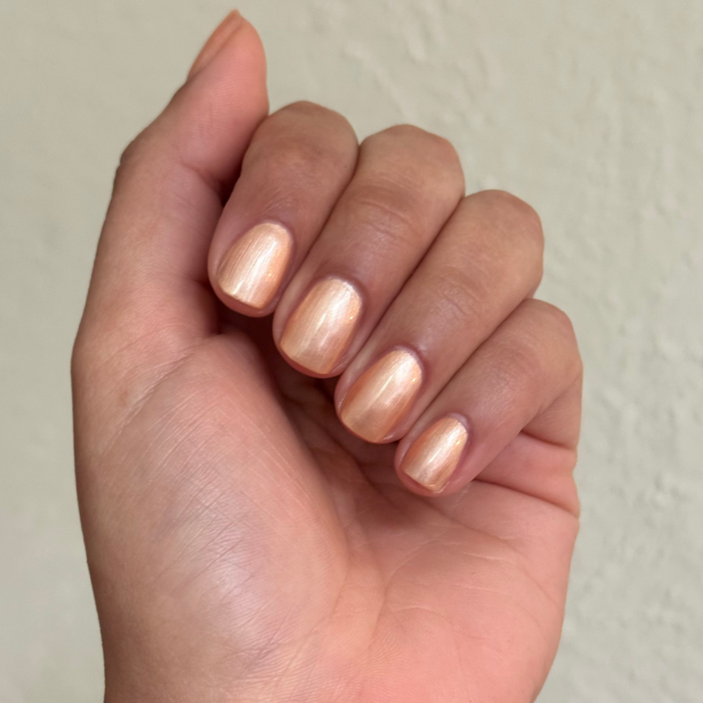 Fingernails painted with Sunlit warm golden peach shimmer gel polish in a natural short rounded shape.