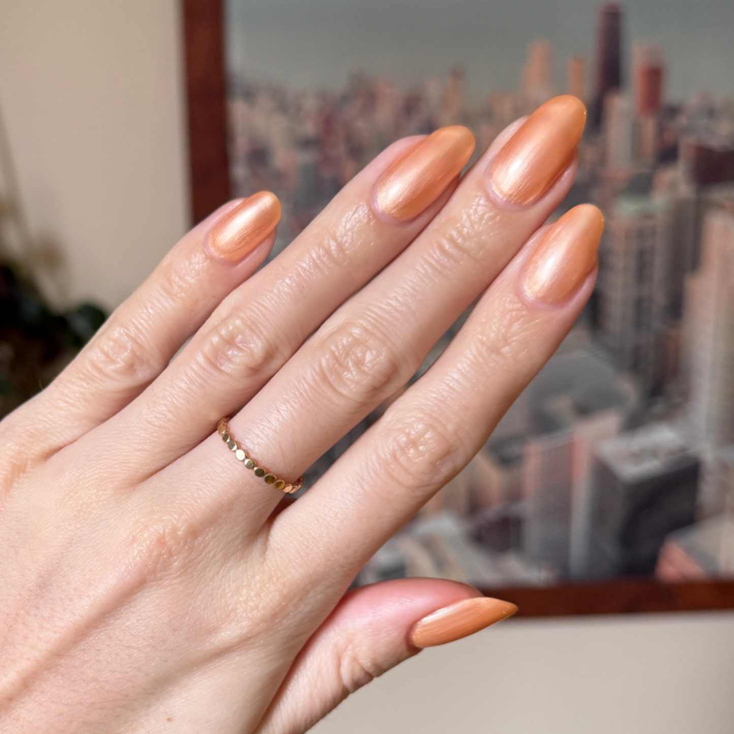 Hand with medium-length nails polished in Sunlit warm golden peach shimmer gel polish against blurred cityscape background