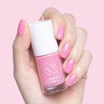Hand holding Olive and June Taffy quick dry nail polish bottle with bright pink nails against pale pink background